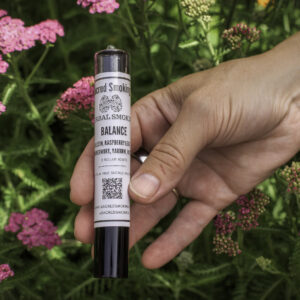 hand holding a tube of rolled joints in a bush of yarrow